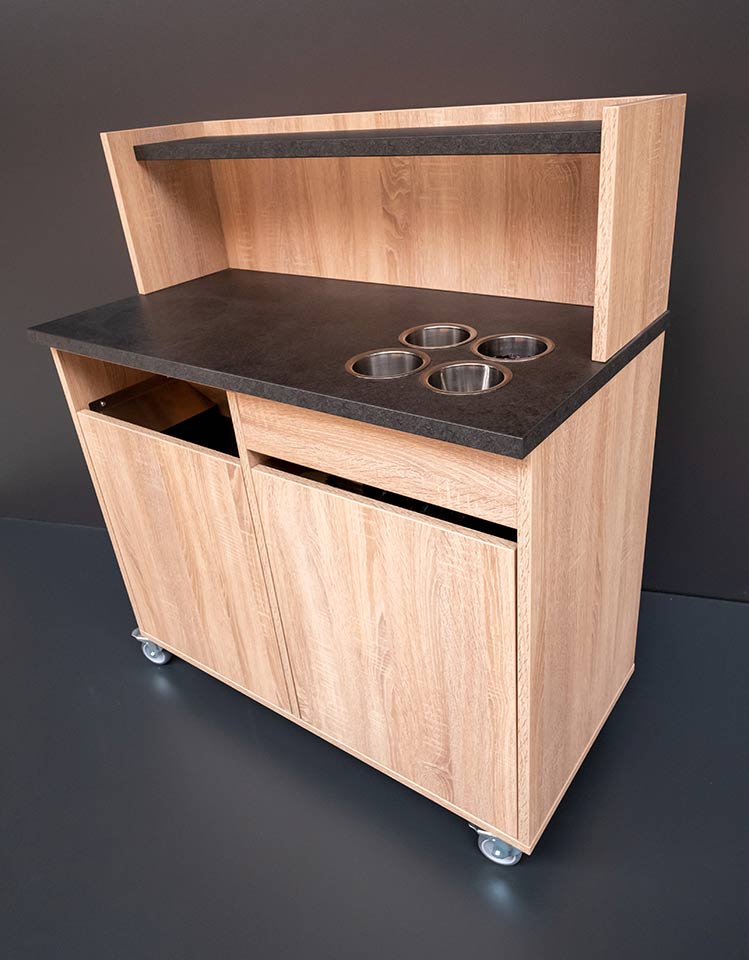 Mobiler Holz-Unterschrank mit schwarzer Arbeitsplatte, vier Edelstahlbechern und Ablageboard.