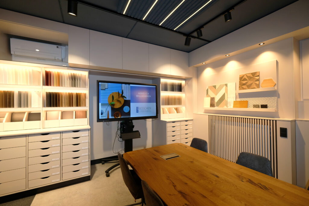 Modern gestalteter Besprechungsraum mit Musterschränken, Holzdekorproben und großem Bildschirm.