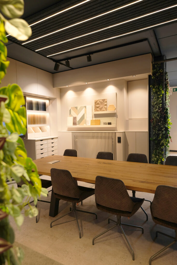 Stilvoller Besprechungsbereich mit großem Holztisch, gepolsterten Stühlen, Musterpräsentation an der Wand und integrierter Beleuchtung.