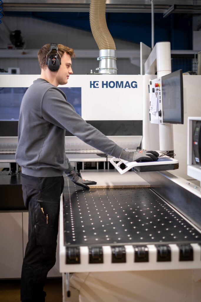 Ein Mitarbeiter bedient eine CNC-Holzbearbeitungsmaschine der Marke Homag in einer Werkstatt.