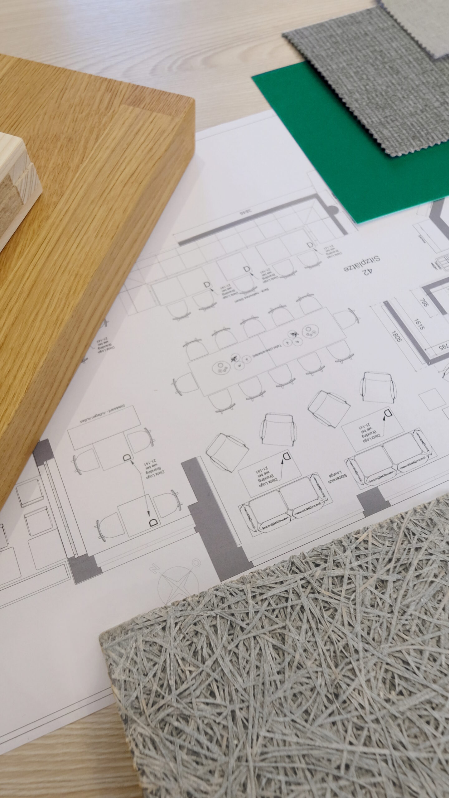 Innenarchitektonisches Planungsszenario mit Möblierungsplan, Holz- und Stoffmustern sowie strukturiertem Akustikpaneel auf einem hellen Tisch.