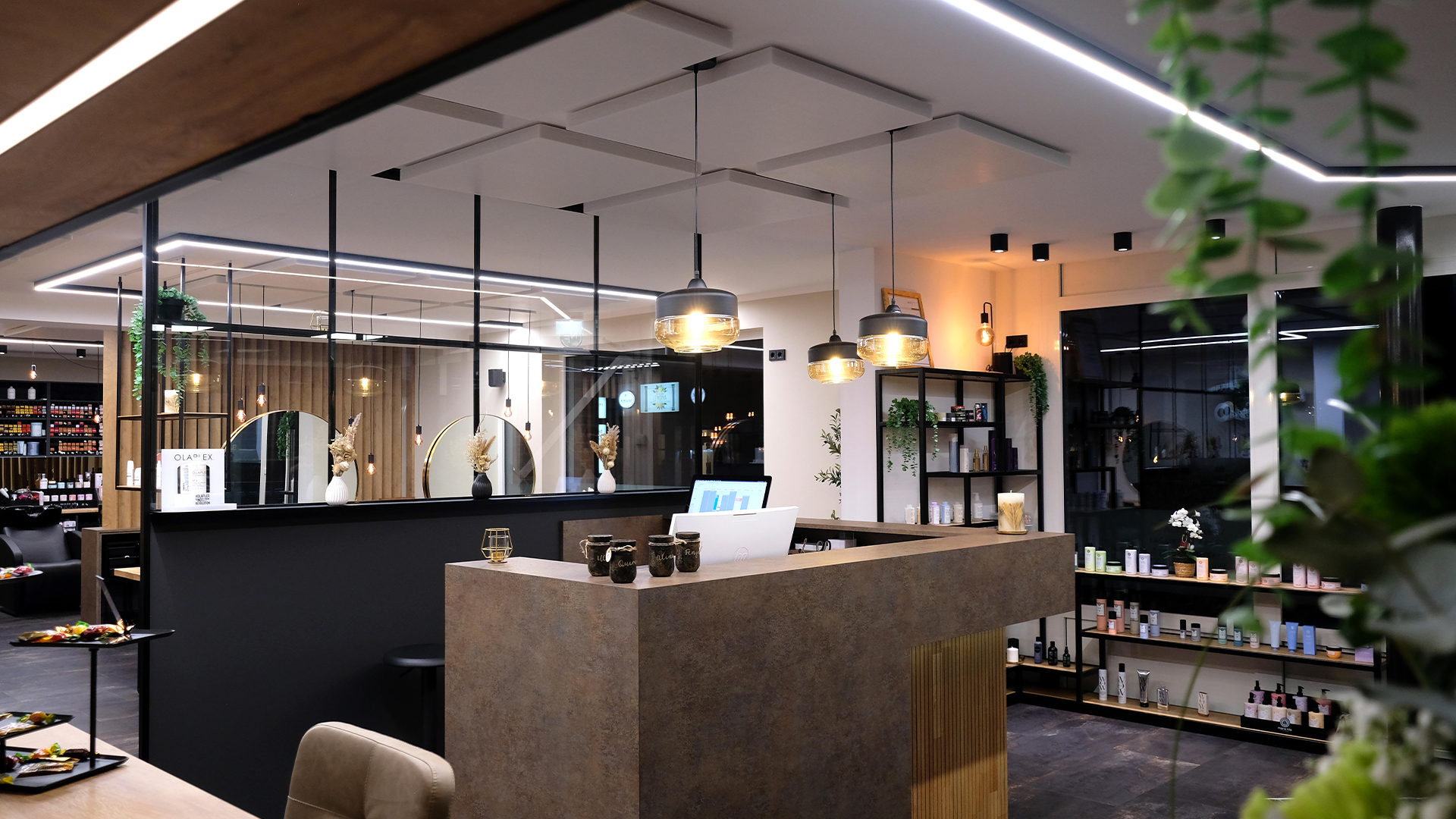 Empfangsbereich eines modernen Friseursalons in Ottersberg mit einem tollen in Steinoptik beleuchteten Tresen. Große golden Spiegel und einladene Sitzbereiche für die Kunden. Ein individuell gestaltetes Regal in schwarzem Metall für angebotene Pflegeprodukte ist im Hintergrund zu sehen.